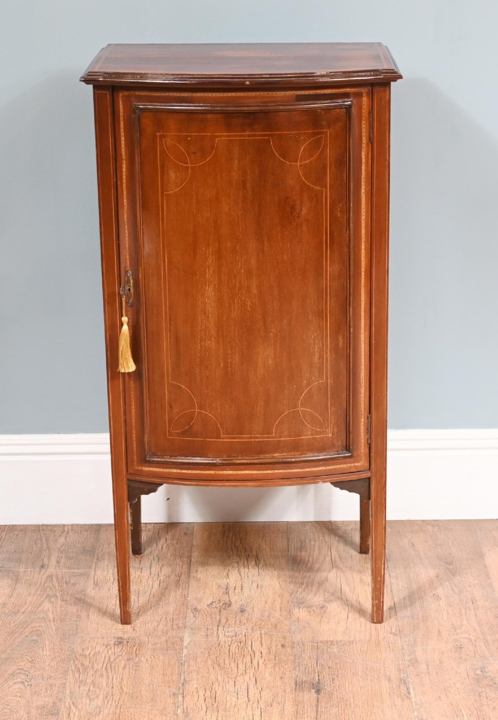 A late Victorian bow-fronted mahogany side cabinet with delicate boxwood line inlay, a single door with key, and slender square tapered legs.