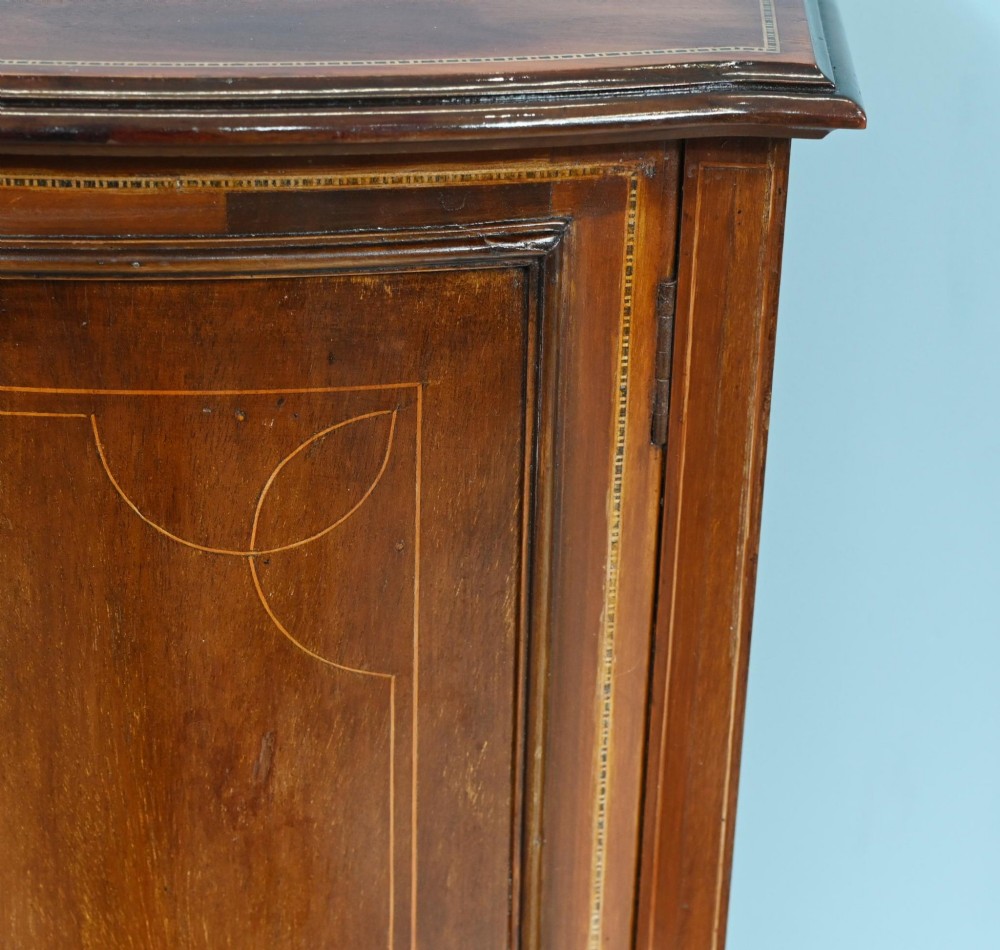 A late Victorian bow-fronted mahogany side cabinet with delicate boxwood line inlay, a single door with key, and slender square tapered legs. View V