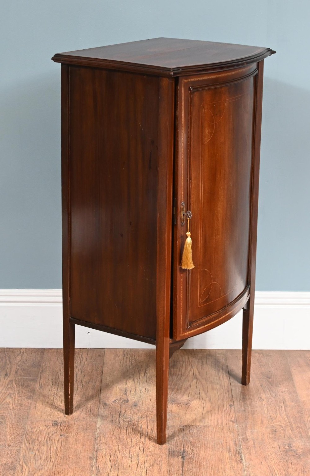 A late Victorian bow-fronted mahogany side cabinet with delicate boxwood line inlay, a single door with key, and slender square tapered legs. View VI