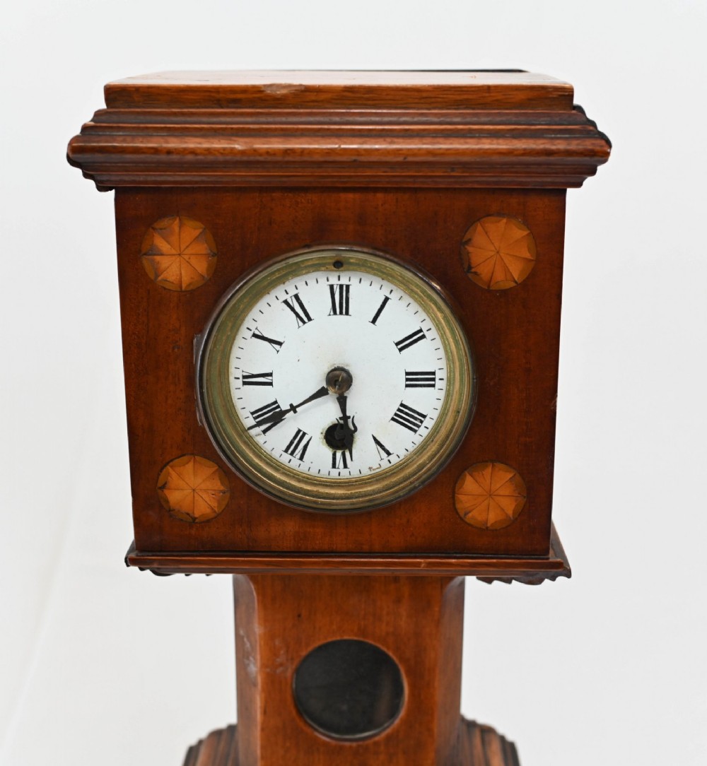 A miniature mahogany longcase clock featuring classical Sheraton style wood inlay with an urn motif and a circular white dial with Roman numerals. View III
