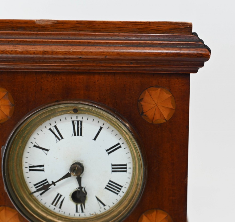 A miniature mahogany longcase clock featuring classical Sheraton style wood inlay with an urn motif and a circular white dial with Roman numerals. View X