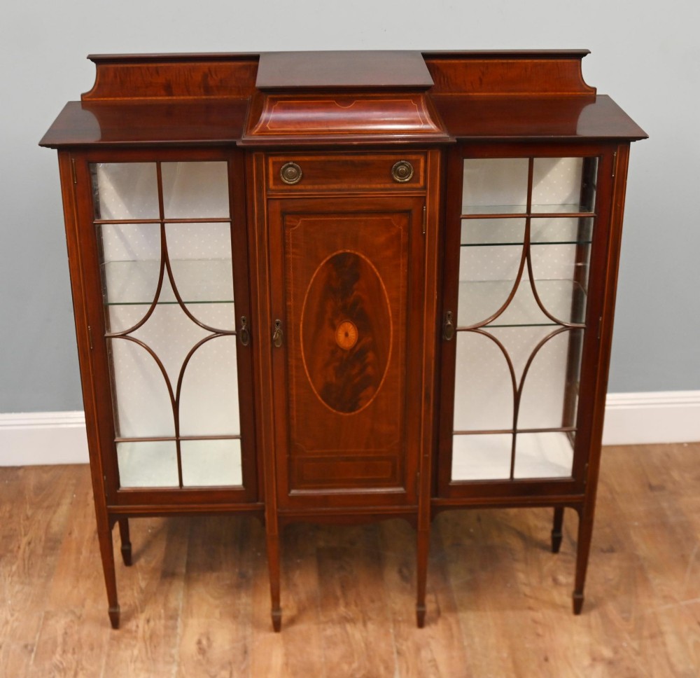 An Edwardian inlaid mahogany display cabinet featuring astragal glazed side doors, a central wooden cupboard with oval marquetry, and slender square tapered legs.
