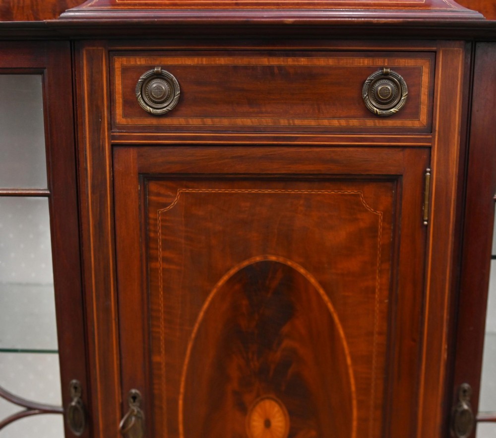 An Edwardian inlaid mahogany display cabinet featuring astragal glazed side doors, a central wooden cupboard with oval marquetry, and slender square tapered legs. View V