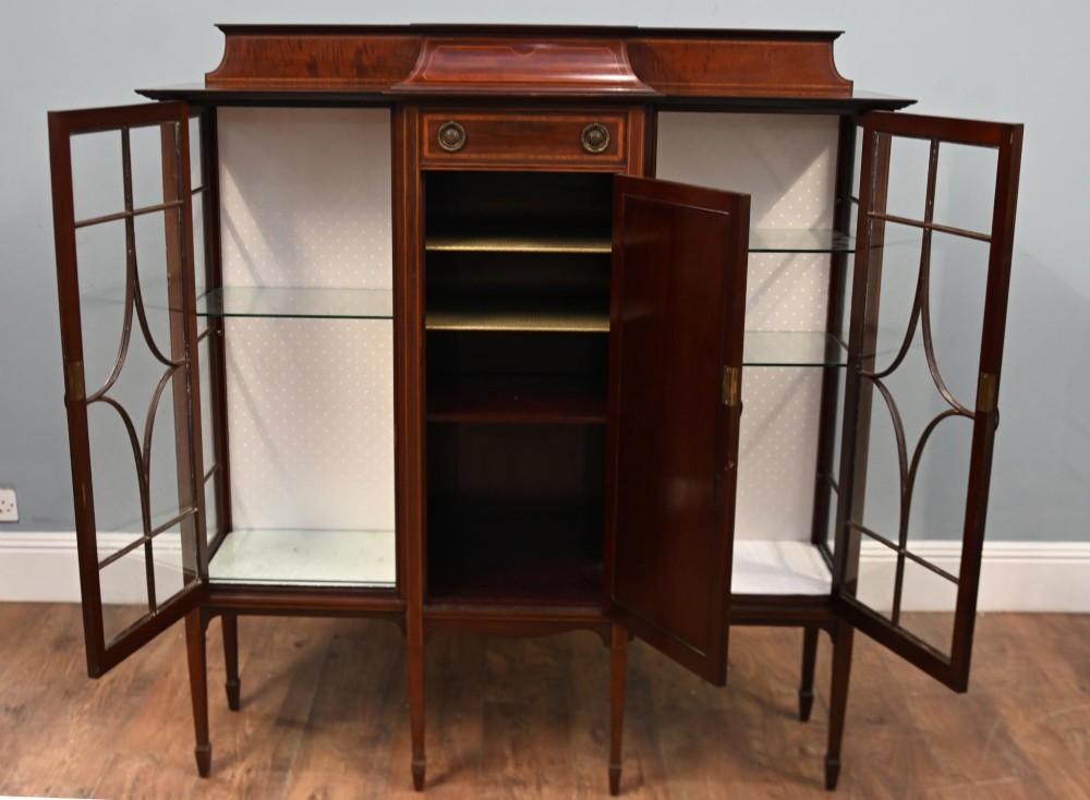An Edwardian inlaid mahogany display cabinet featuring astragal glazed side doors, a central wooden cupboard with oval marquetry, and slender square tapered legs. View VIII