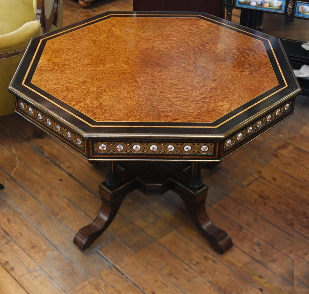 An octagonal Victorian centre table crafted from burr amboyna wood with ebonised borders and an apron decorated with porcelain roundels.