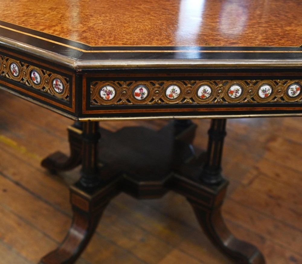 An octagonal Victorian centre table crafted from burr amboyna wood with ebonised borders and an apron decorated with porcelain roundels. View V