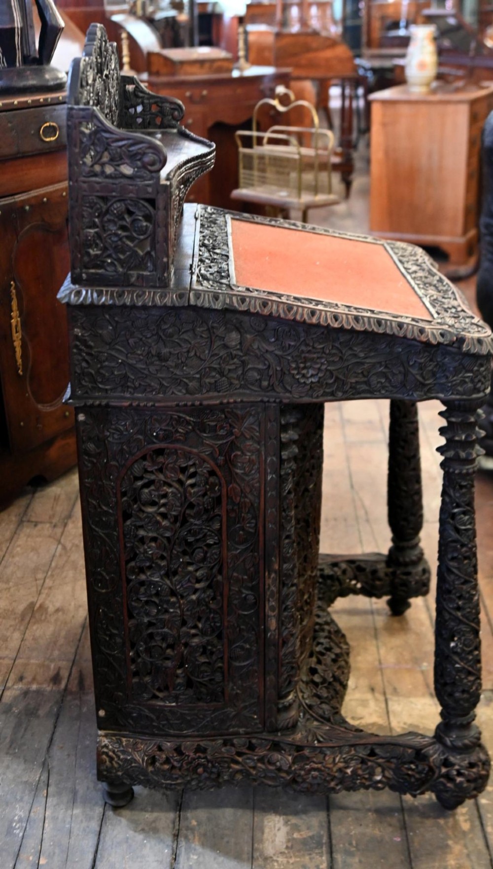 A dark hardwood Burmese Davenport desk with pierced carved floral decoration, an openwork gallery, and a terracotta leather writing surface. View X