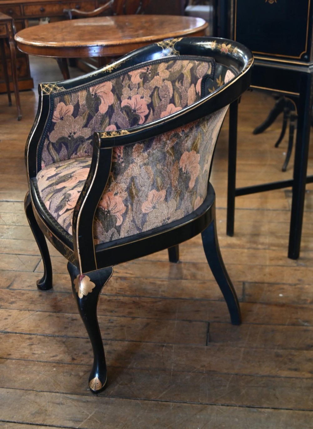 A pair of black lacquered Chinoiserie armchairs featuring hand-painted gold detail, curved backs, pink floral upholstery, and cabriole legs. View V
