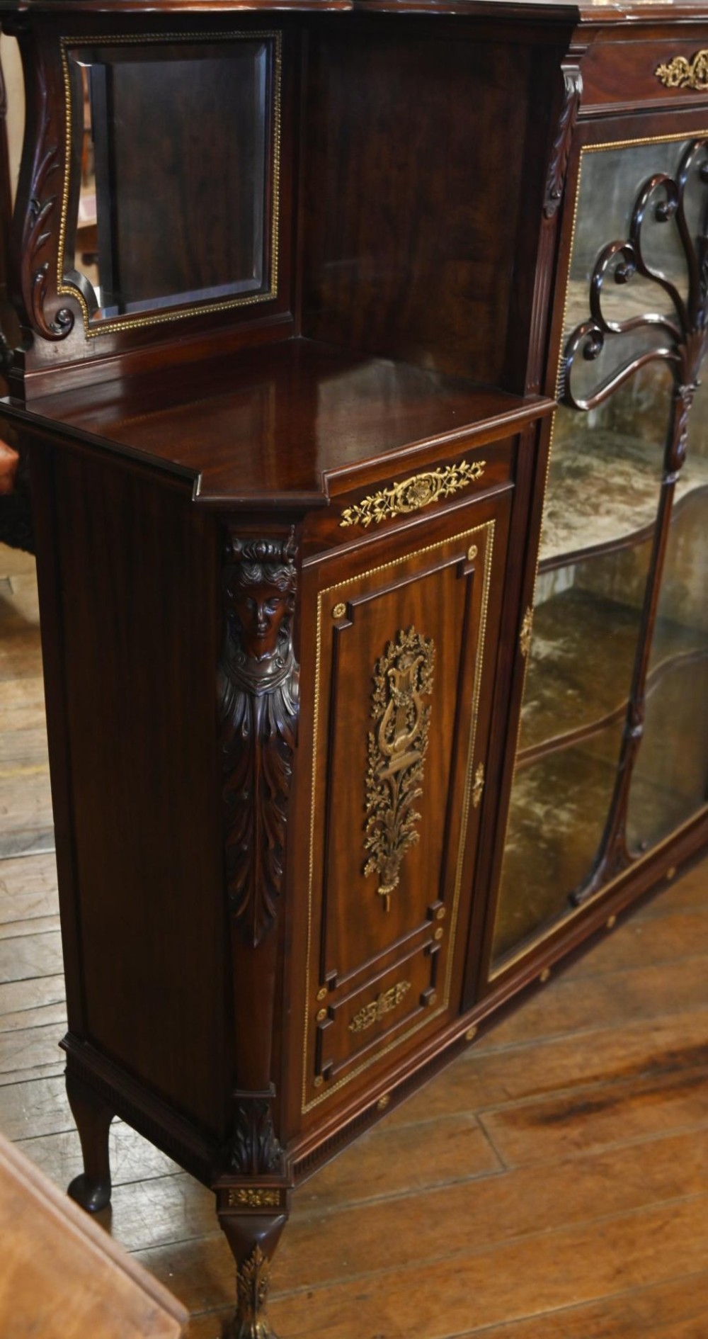 A dark mahogany display cabinet featuring gilt ormolu mounts, bevelled mirror panels, and a central glass door with decorative organic glazing bars. View IV