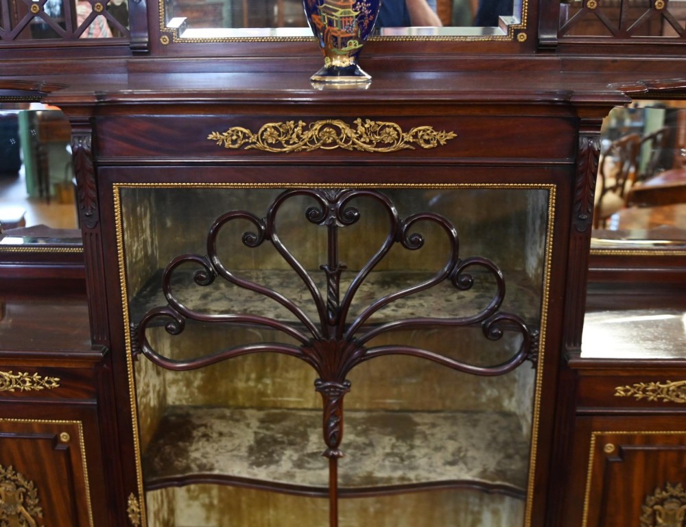 A dark mahogany display cabinet featuring gilt ormolu mounts, bevelled mirror panels, and a central glass door with decorative organic glazing bars. View VI