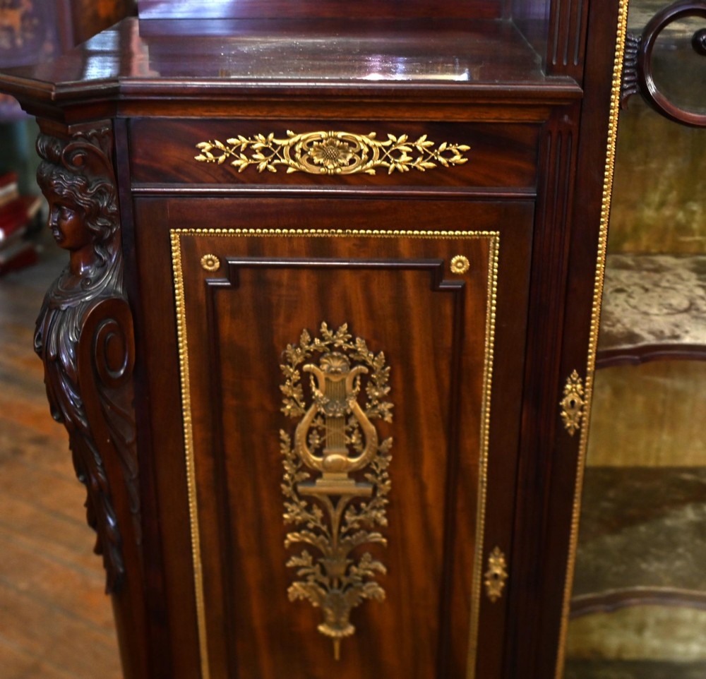 A dark mahogany display cabinet featuring gilt ormolu mounts, bevelled mirror panels, and a central glass door with decorative organic glazing bars. View VII