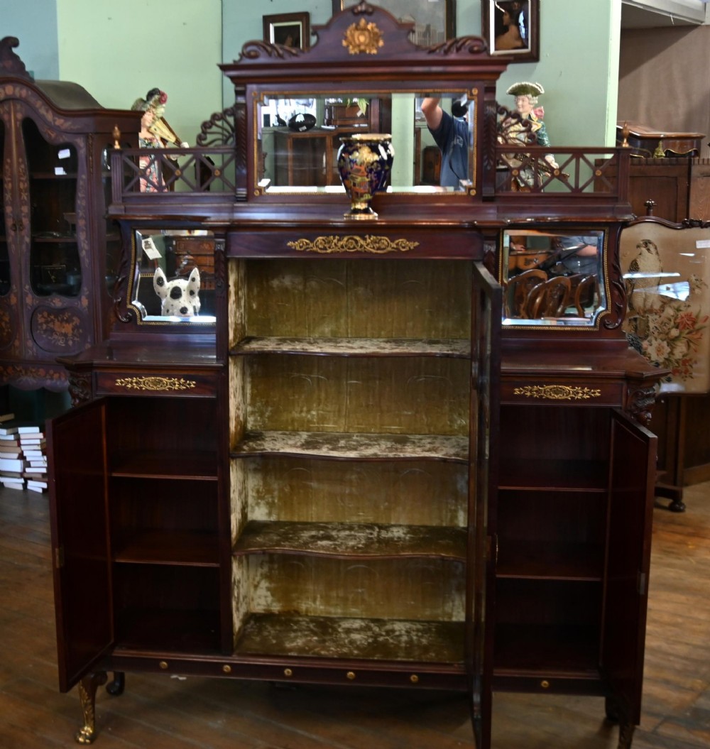 A dark mahogany display cabinet featuring gilt ormolu mounts, bevelled mirror panels, and a central glass door with decorative organic glazing bars. View IX