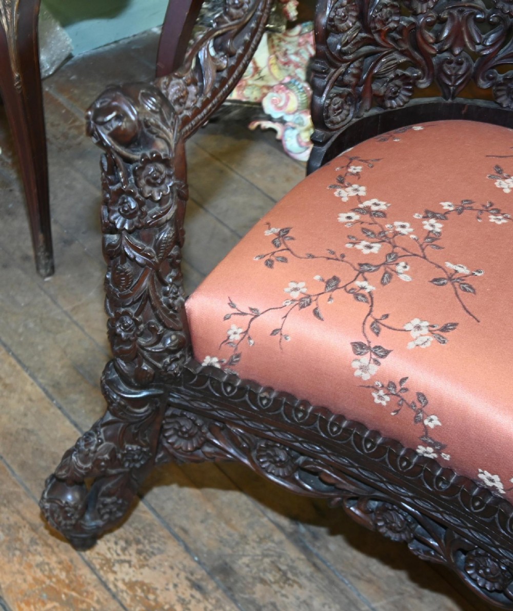An intricately carved 19th-century dark teak sofa featuring openwork floral motifs and a terracotta floral upholstered seat pad. View II