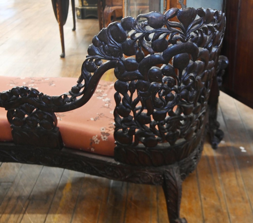 An intricately carved 19th-century dark teak sofa featuring openwork floral motifs and a terracotta floral upholstered seat pad. View VII