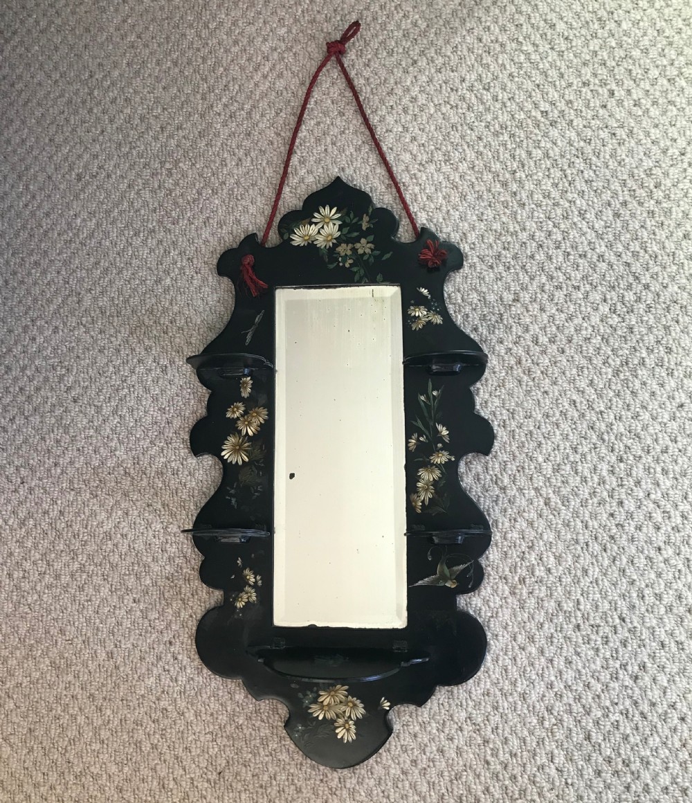 A Victorian ebonised wooden wall mirror featuring small tier display shelves and hand-painted white floral and bird motifs around a central rectangular mirror plate.