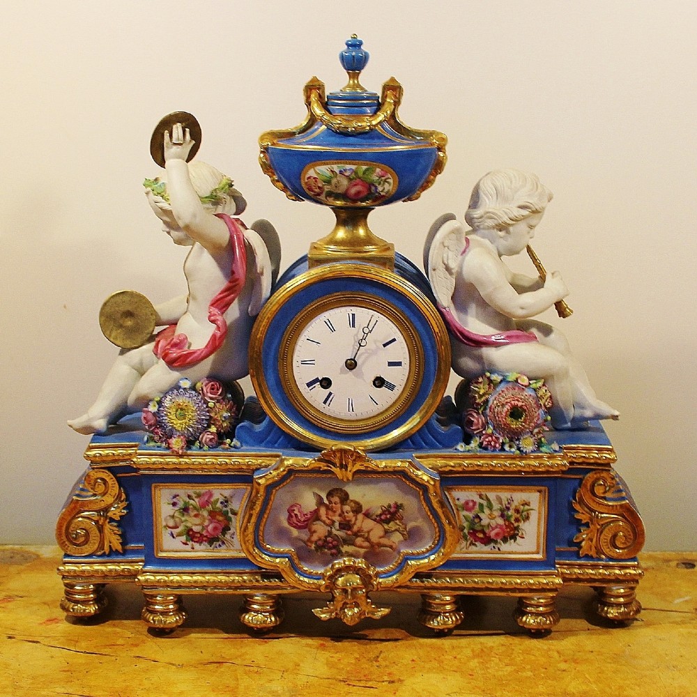 An antique French Sevres-style porcelain mantel clock featuring cobalt blue glaze, hand-painted floral panels, gilt bronze mounts, and two sculpted cherub figures flanking the dial.