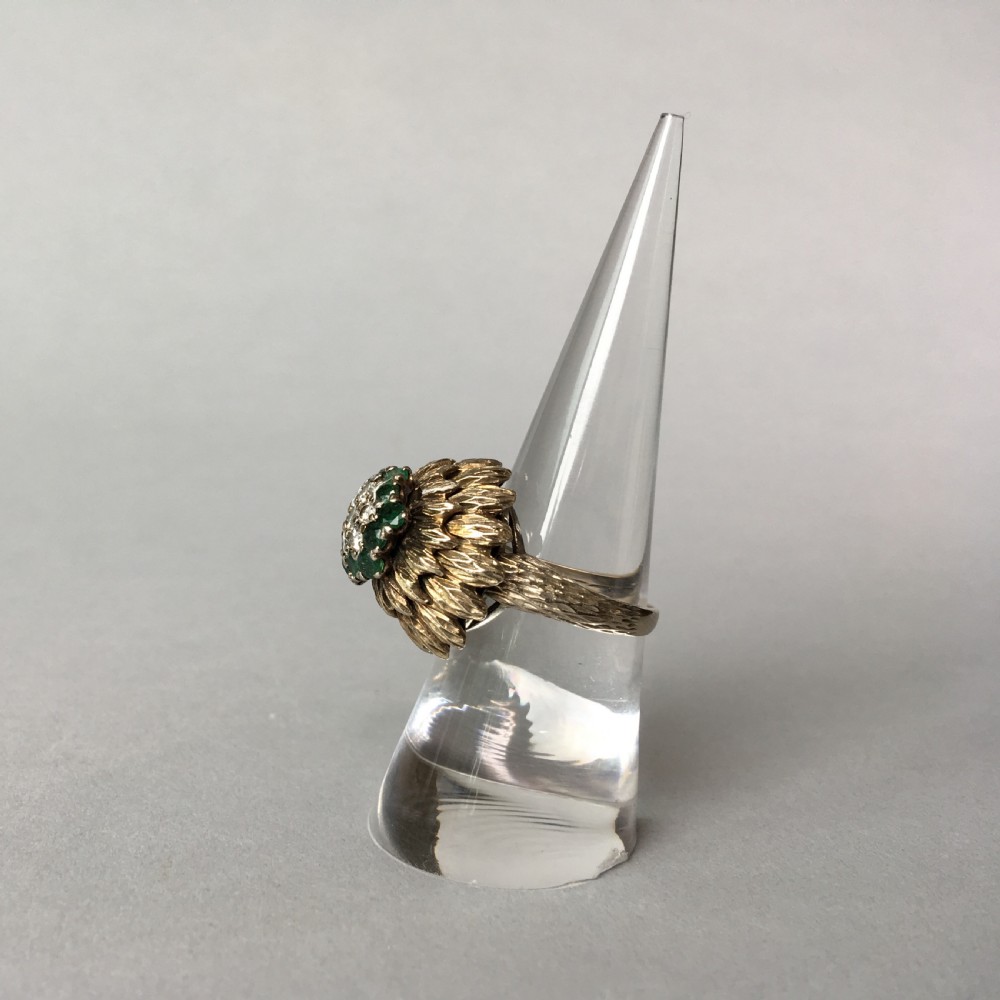 A textured yellow gold cocktail ring featuring a central cluster of round brilliant diamonds surrounded by emeralds and feathered metalwork. View III