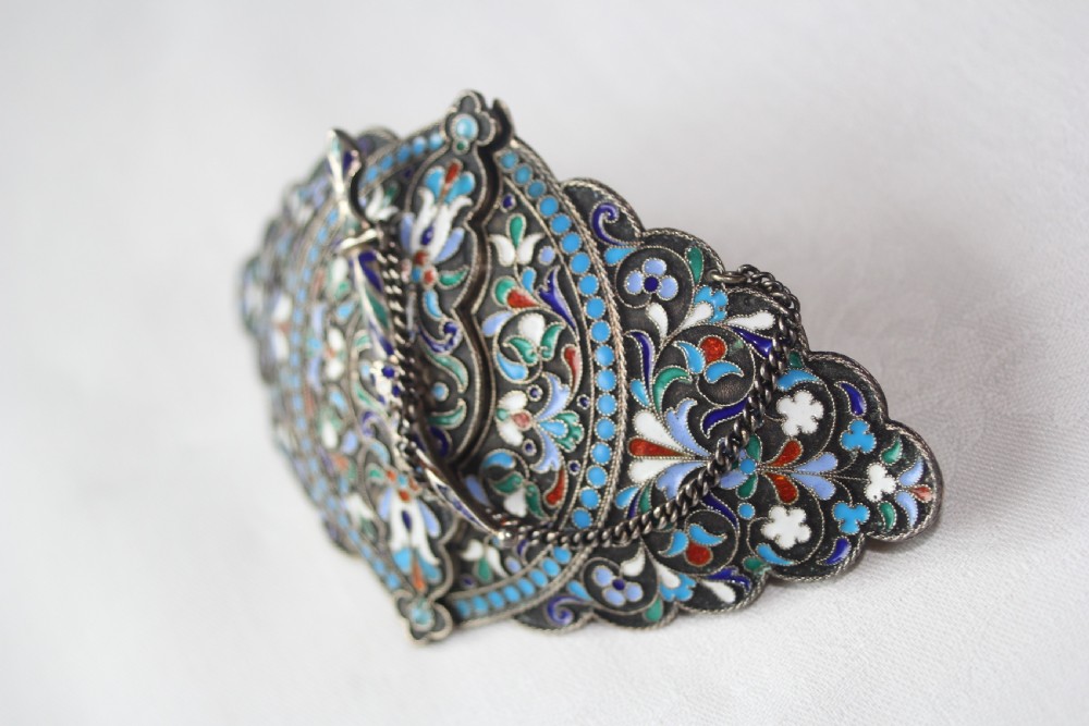 A lobed silver belt buckle decorated with intricate polychrome floral cloisonne enamel in shades of turquoise, navy, white, and green, complete with a small dagger-shaped fastening pin. View II