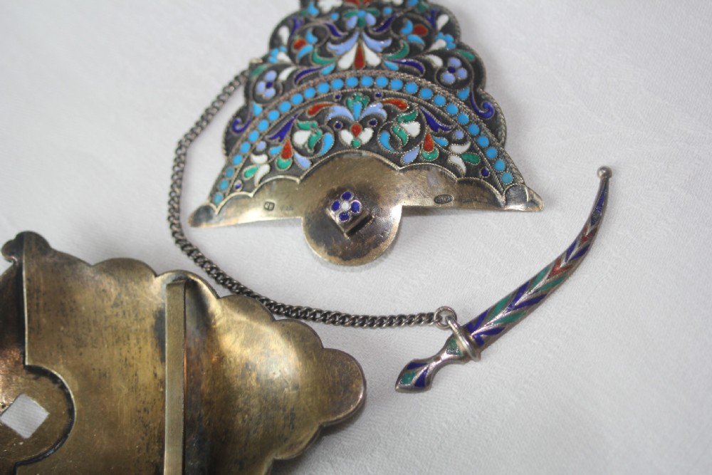 A lobed silver belt buckle decorated with intricate polychrome floral cloisonne enamel in shades of turquoise, navy, white, and green, complete with a small dagger-shaped fastening pin. View III