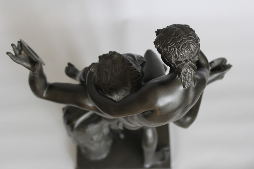A dark patinated bronze sculpture depicting a male faun holding cymbals with the infant Bacchus seated on his shoulders, mounted on a rectangular plinth base. View III