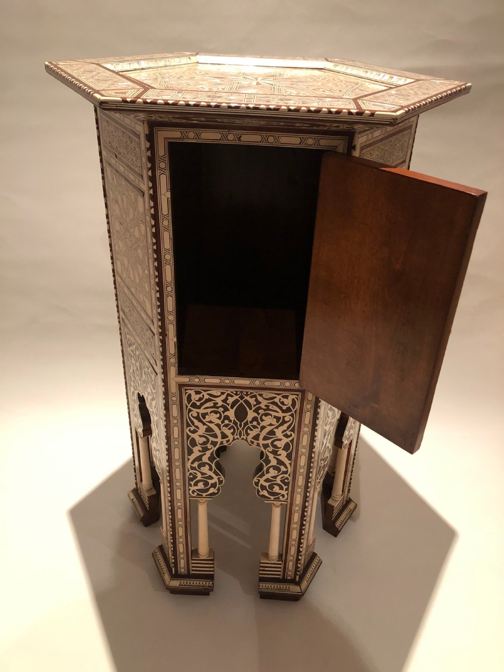 An octagonal dark wood side table with intricate bone and mother-of-pearl geometric inlay, featuring carved horseshoe arches and turned legs at the base. View III