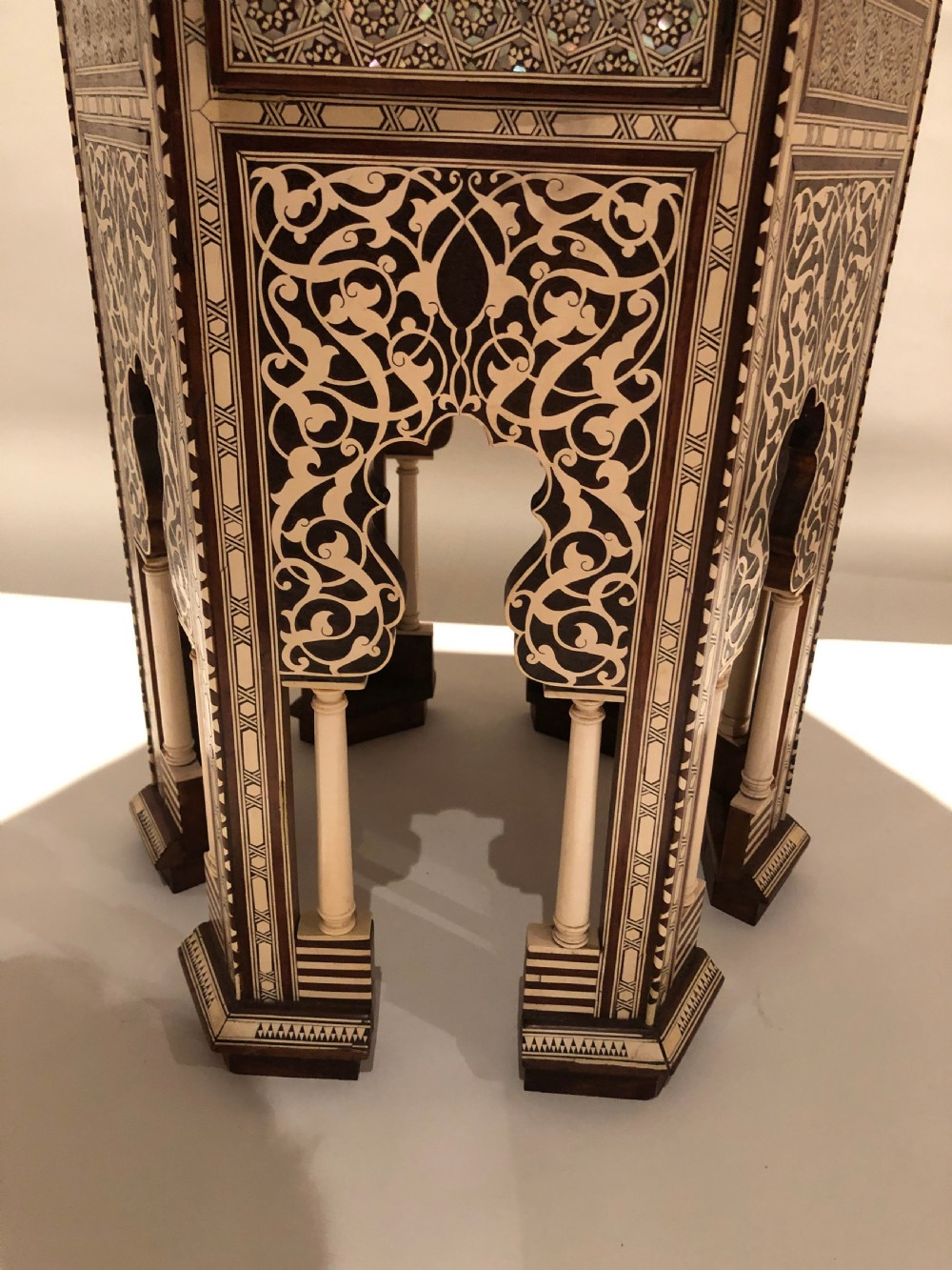 An octagonal dark wood side table with intricate bone and mother-of-pearl geometric inlay, featuring carved horseshoe arches and turned legs at the base. View IV