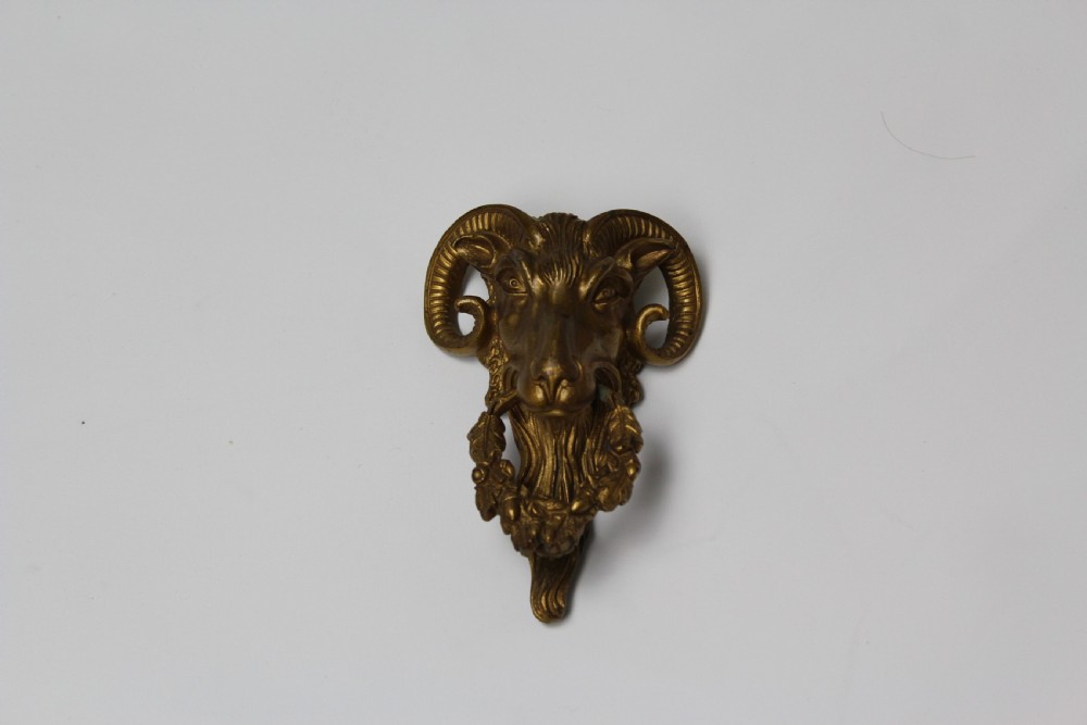A 19th-century cast brass rams head mount with curved horns and a wreath of leaves in its mouth.