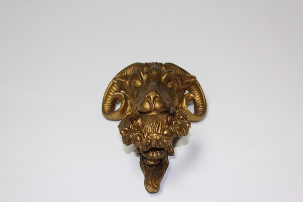 A 19th-century cast brass rams head mount with curved horns and a wreath of leaves in its mouth. View II