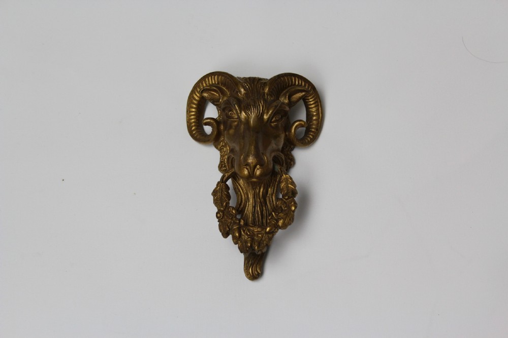A 19th-century cast brass rams head mount with curved horns and a wreath of leaves in its mouth. View III