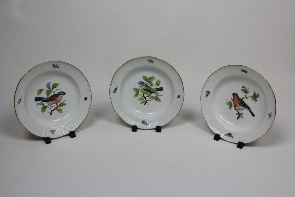 A set of three circular white porcelain dessert dishes featuring hand-painted birds and insects with basketweave moulded rims and gilt borders.