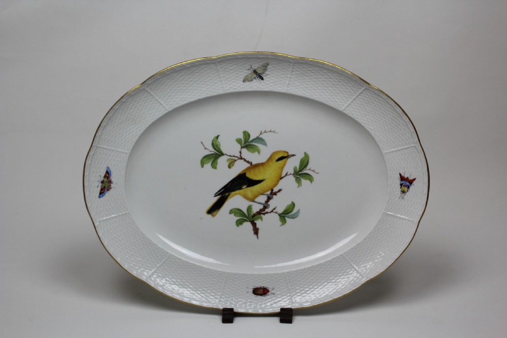 An oval white porcelain serving platter featuring a hand-painted yellow bird on a branch in the centre, surrounded by insect motifs on a basketweave rim with a gold edge.