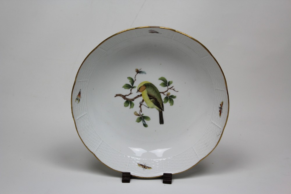 A circular white porcelain bowl featuring hand-painted bird and insect motifs with a basketweave embossed border and gilded rim.