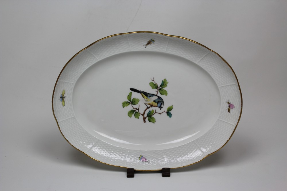 An oval white hard-paste porcelain platter featuring a hand-painted songbird on a branch in the centre, surrounded by painted insects and a gilded rim with a relief basketweave border.