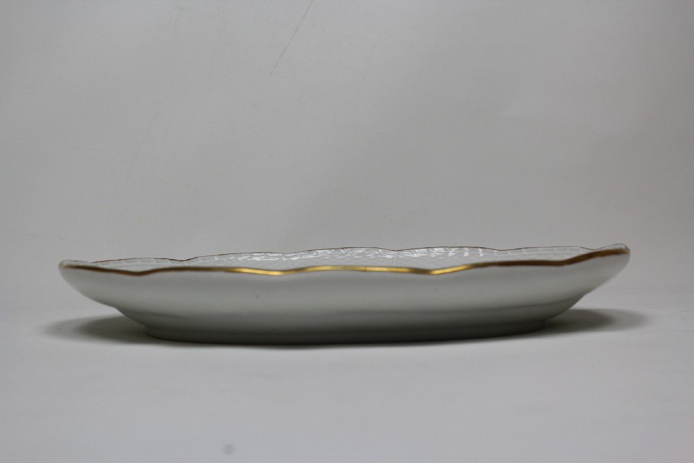 An oval white hard-paste porcelain platter featuring a hand-painted songbird on a branch in the centre, surrounded by painted insects and a gilded rim with a relief basketweave border. View II