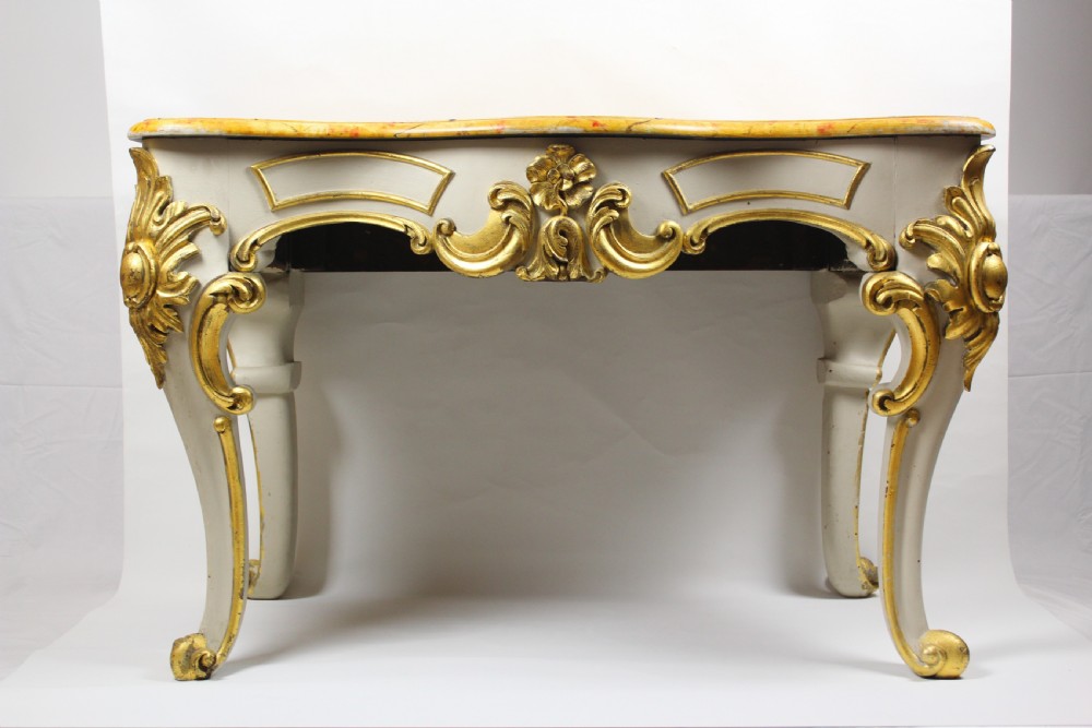 A French Rococo style console table featuring an off-white painted frame with gilded leaf carvings, cabriole legs, and a yellow Sienna marble top.