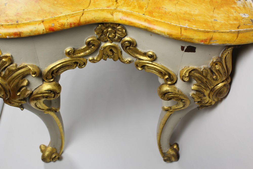A French Louis XV style console table featuring a serpentine yellow sienna marble top over a grey painted frame decorated with giltwood acanthus carvings. View IV