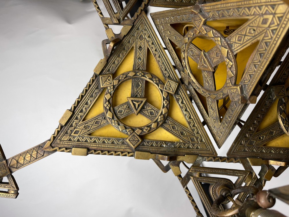 An Arts and Crafts style brass seven-light chandelier featuring geometric framework and suspended red and green glass cups. View VI