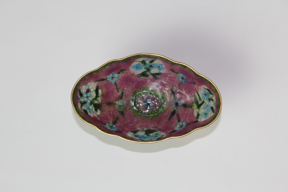 A footed plique-a-jour enamel bowl featuring a pink geometric background with blue floral medallions and gilt metal rim. View II