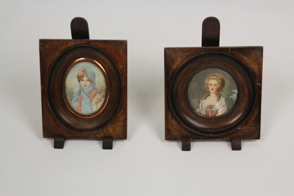 A pair of antique square dark wood framed portrait miniatures depicting two women dressed in historical attire.