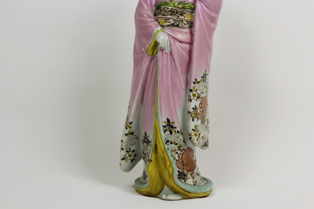 A hand-painted porcelain figurine of a Japanese geisha wearing a pink floral kimono with hand resting near her chin. View III