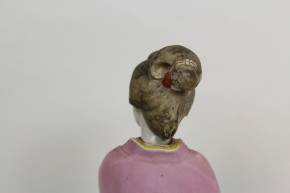 A hand-painted porcelain figurine of a Japanese geisha wearing a pink floral kimono with hand resting near her chin. View VI
