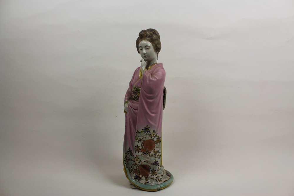 A hand-painted porcelain figurine of a Japanese geisha wearing a pink floral kimono with hand resting near her chin. View VII