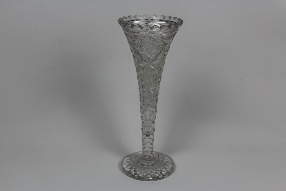 A tall trumpet-shaped clear hand-cut crystal vase featuring diamond cuts, a scalloped top rim, and a circular starburst pattern base. View III