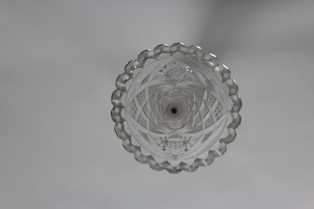 A tall trumpet-shaped clear hand-cut crystal vase featuring diamond cuts, a scalloped top rim, and a circular starburst pattern base. View IV