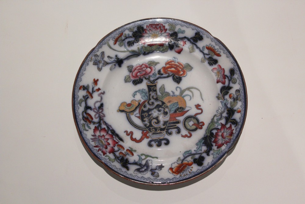 A circular Victorian ceramic plate featuring a central motif of a vase with flowers surrounded by a floral rim on a white glazed surface.