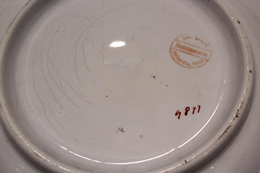 A round 19th-century cream ceramic plate with hand-painted floral motifs, a moulded rim, and black German text written in Fraktur script in the centre. View IV