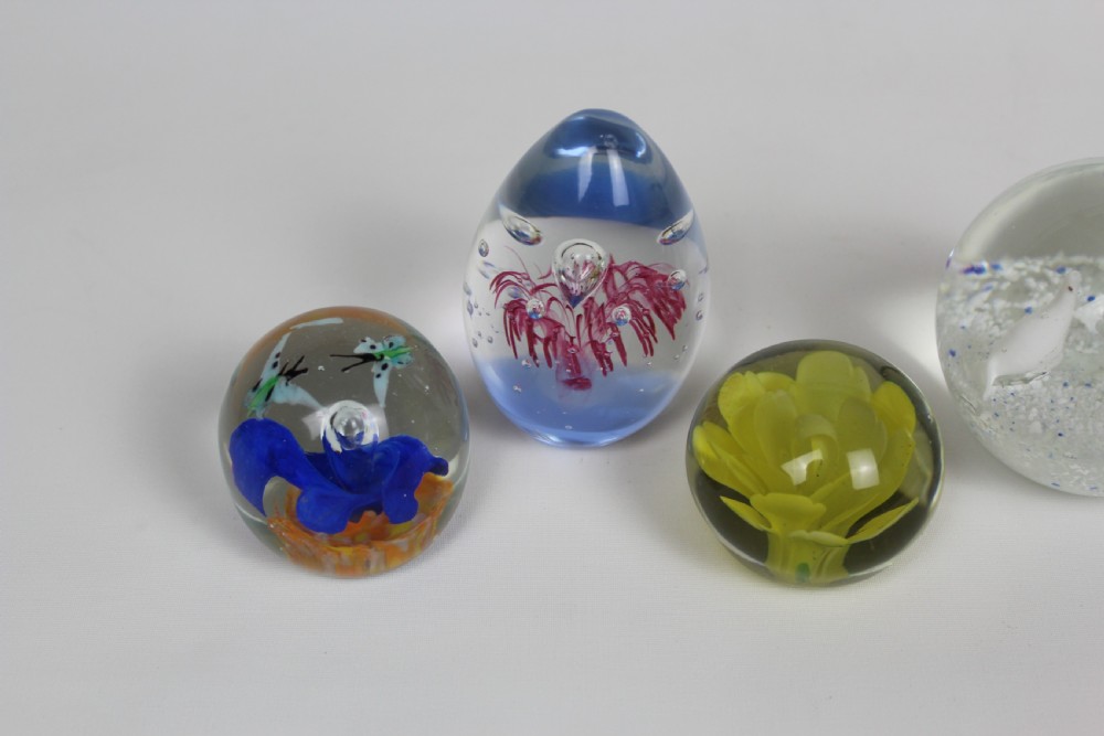 A collection of six assorted glass paperweights featuring various internal floral motifs, colourful swirls, and controlled bubbles. View II