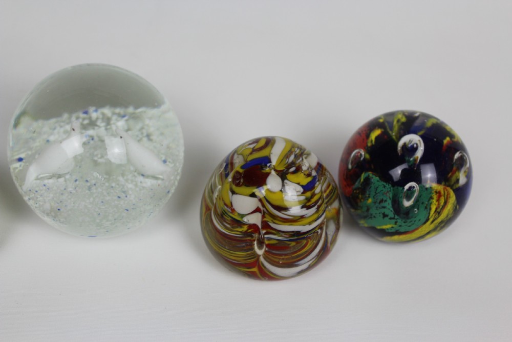 A collection of six assorted glass paperweights featuring various internal floral motifs, colourful swirls, and controlled bubbles. View III