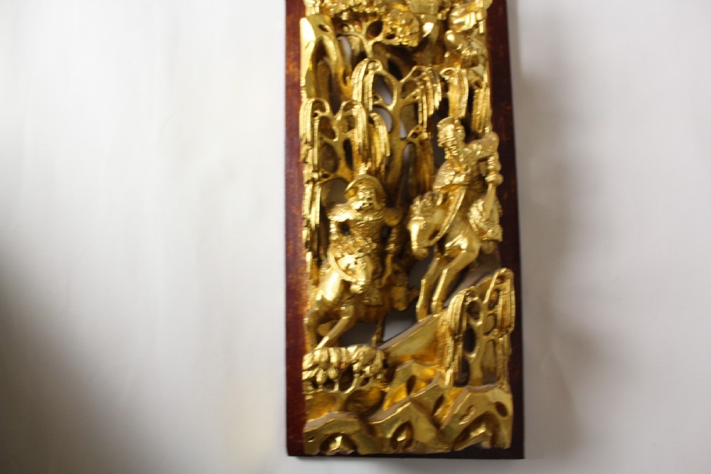 An elongated rectangular Chinese wooden wall plaque featuring deeply carved figures coated in gold leaf mounted on a red backing. View XI
