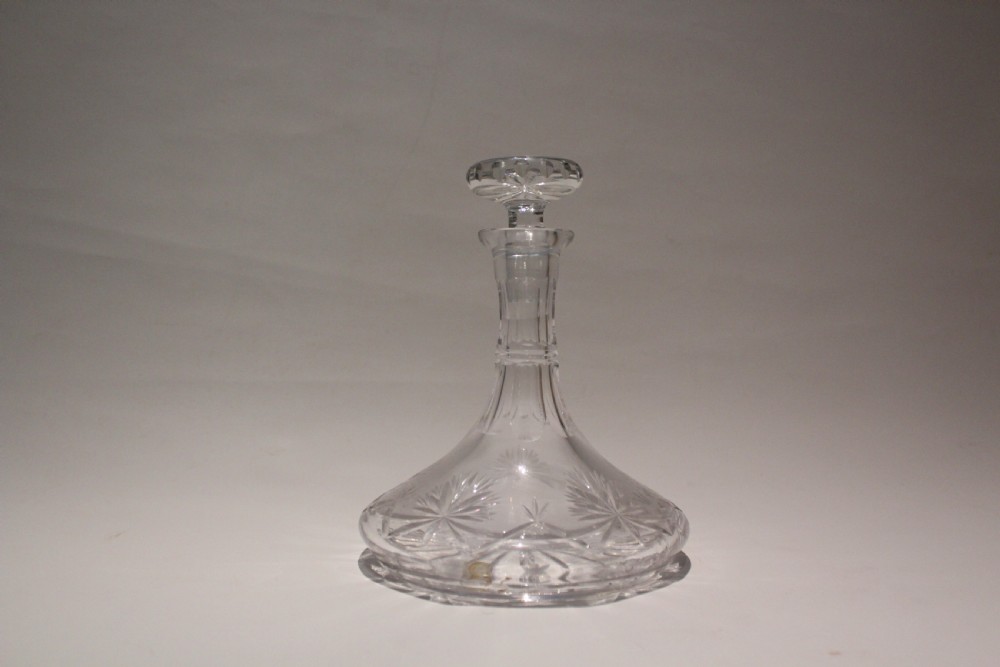 A clear cut-crystal ship decanter with a broad flared base, faceted neck, starburst engravings, and a matching round glass stopper.